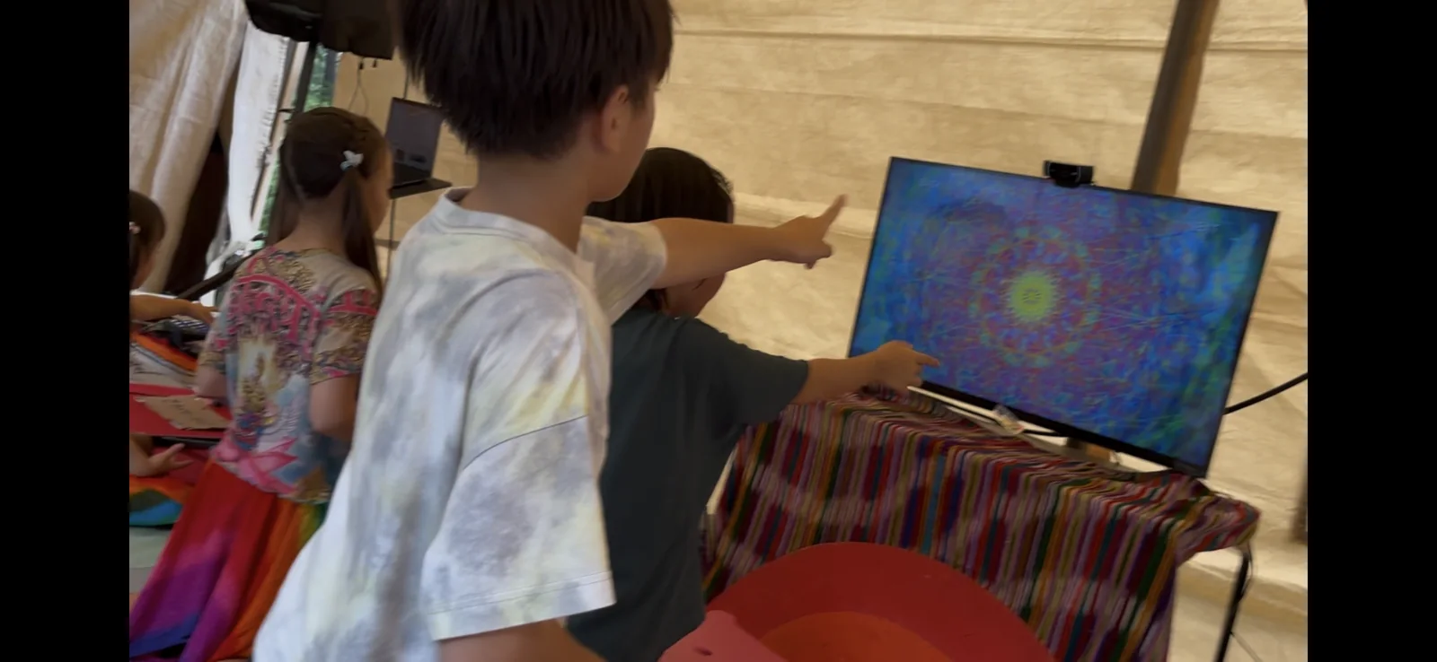 参加者が画面へ手を伸ばし、実機に映るカラフルな模様を体験している様子